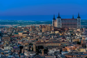 Toledo, Spain at night during the blue hour with the lights of the city flickering.