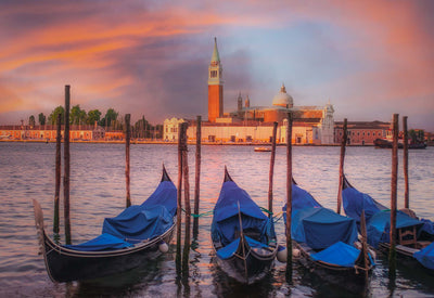 Sunrise on the Grand Canal in Venice, Italy with blue condolas in the foreground.