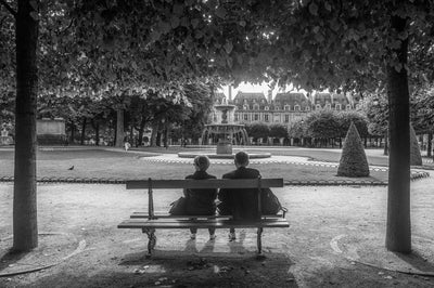 Older couple sitting on a park bench in a Parisian park.