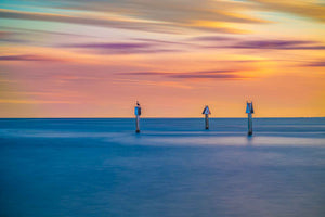 Photo captured at Biscayne Bay that is dream-like with hues of orage and purple in the sky and three channel markers distinctly in focus.
