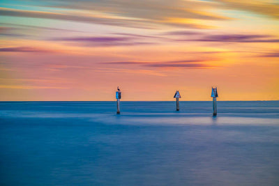 Photo captured at Biscayne Bay that is dream-like with hues of orage and purple in the sky and three channel markers distinctly in focus.