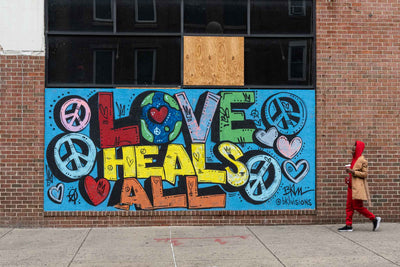 Wall art in Philadelphia that says Love Heals All with a passerby in a red outfit.