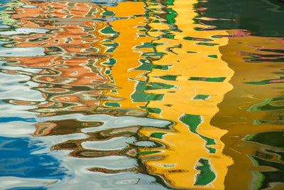 Ripples in a canal in Burano, Italy with colorful reflections from the buildings that line the canal.