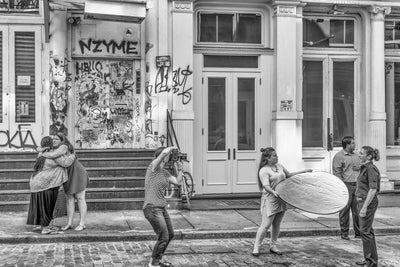 A black and white image captured in New York of a bustling city scene, with people engaged in a photo shoot and friends embracing.