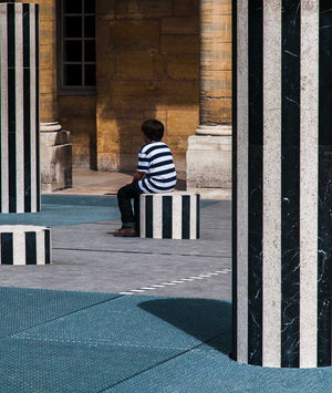 Boy at Palais Royal in Paris sitting on column with black and white stripes and  noy has on black and white striped shirt.