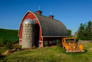 Photo captured in the Palouse of a bright red barn with a very old orange pickup truck in the yard under a deep blue sky.