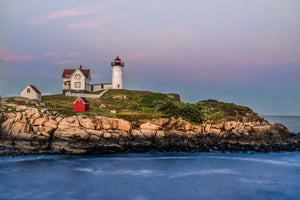 Nubble Lighthouse in York, Maine. The sky is beautiful pink and the white lighthouse sits on its own rocky island. The photo was taken at sunset.