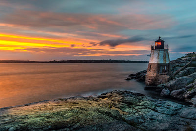 The Castle Hill Lighthouse in Newport, Rhode Island during a beautifule sunset with orange yellow and pink colors in the sky.